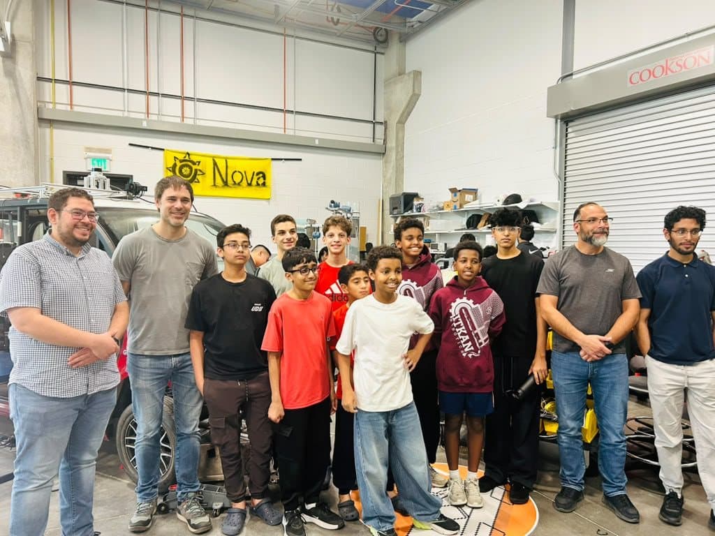 Students and adults in a UT Dallas garage beneath a yellow NOVA banner