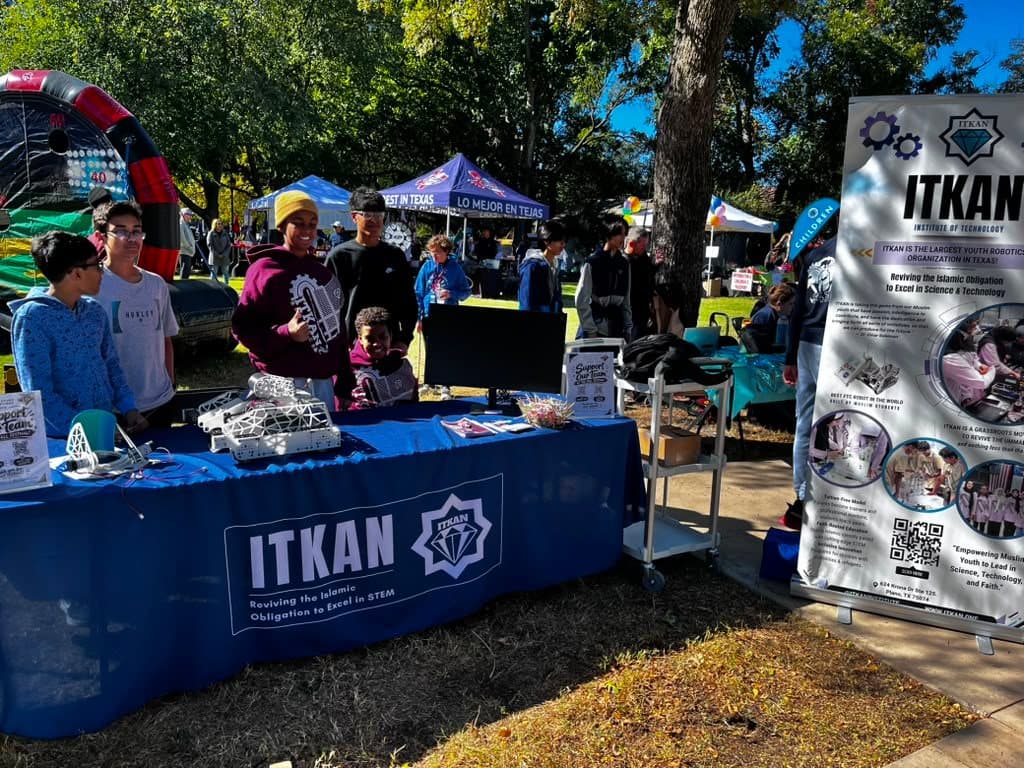 Students at the ITKAN booth at the Plano International Festival, with a robot on the blue ITKAN table and the ITKAN banner beside it