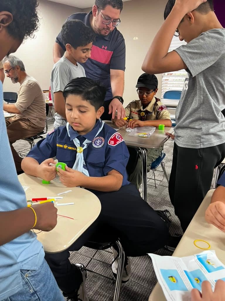 A Cub Scout fits a motor onto his scribble bot while an adult and a team member look on