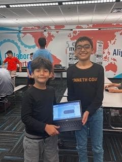 Two Ma'ruf community students stand together holding a laptop showing a design they made