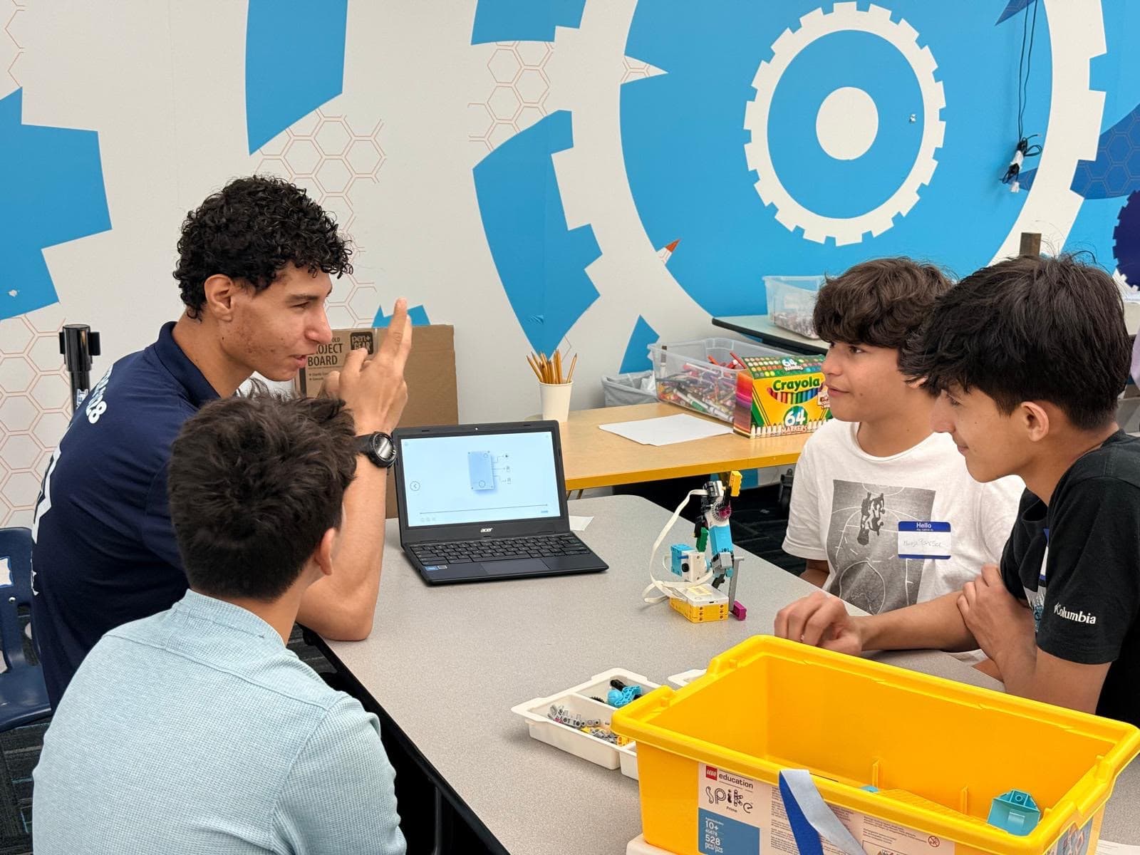 An ITKAN student mentor explains block-based robot programming on a laptop to Ma'ruf students at the Innovation Hub