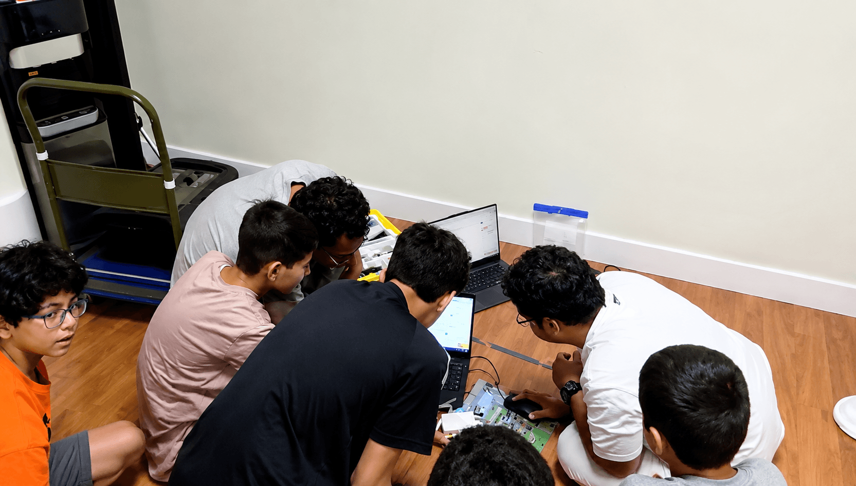 A group of students and a coach sit in a circle working with a laptop and robot components at the Portland pilot session