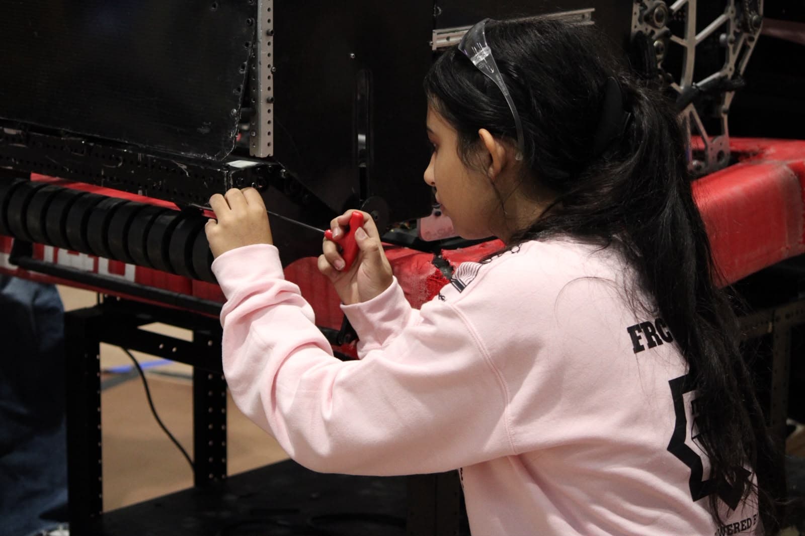 A 10340 team member in safety glasses works on the robot with a screwdriver
