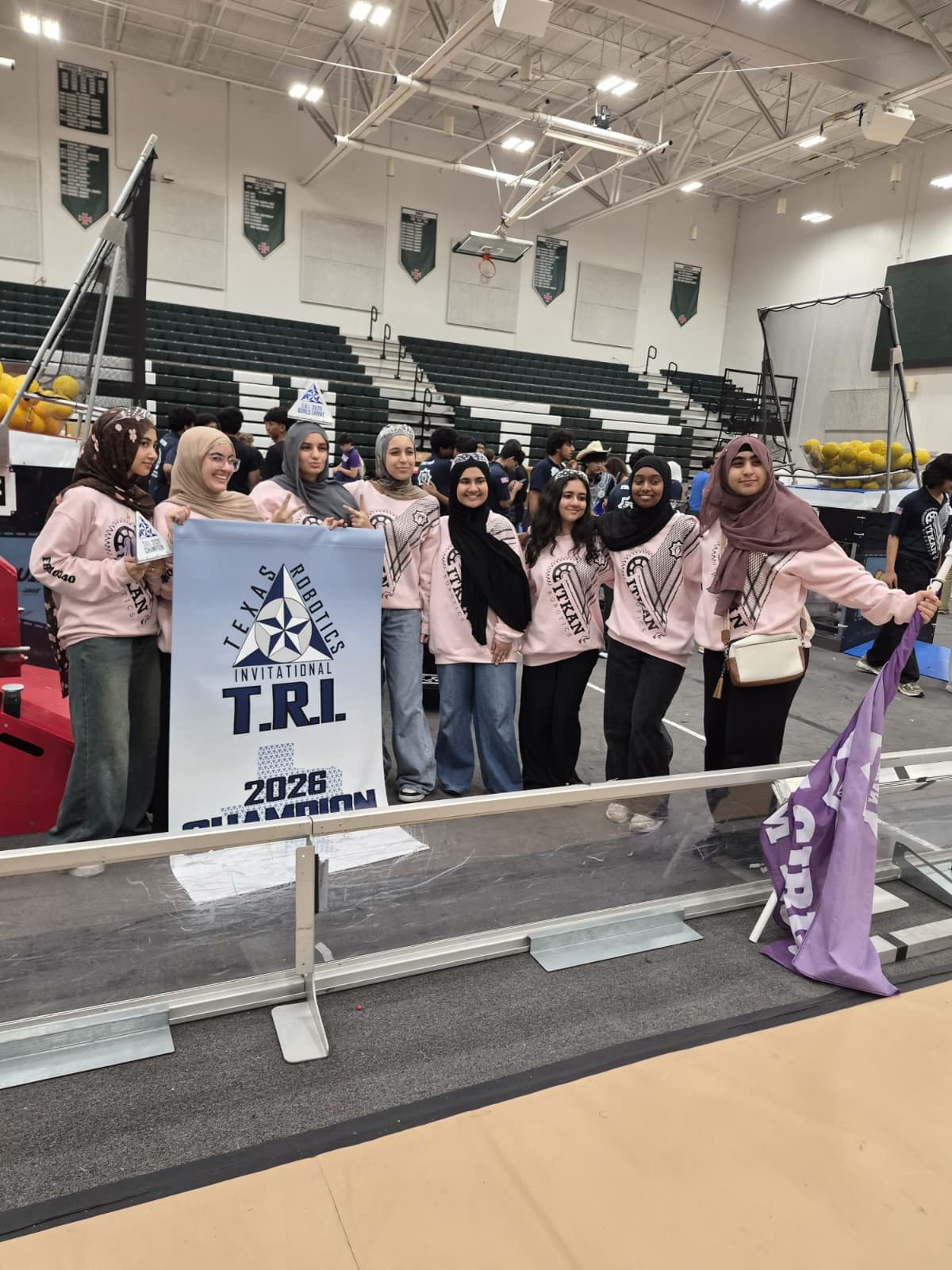 ITKAN Girls 10340 stand at the TRI competition field holding the Texas Robotics Invitational 2026 Champion banner
