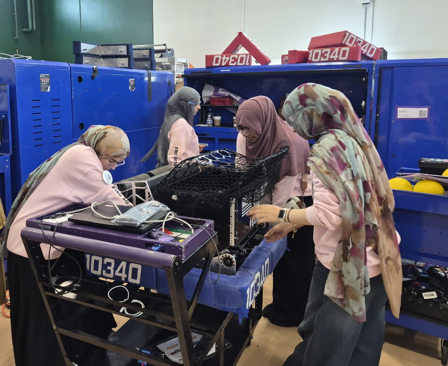 ITKAN Girls 10340 members lean over their robot in the pits at TRI, making last-minute adjustments before a match